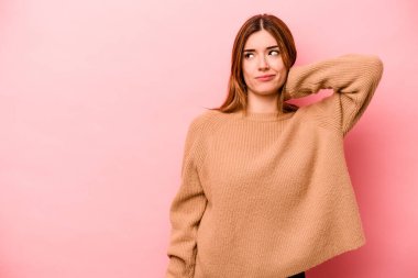 Kafkasyalı genç bir kadın pembe arka planda izole edilmiş kafasının arkasına dokunuyor, düşünüyor ve bir seçim yapıyor..