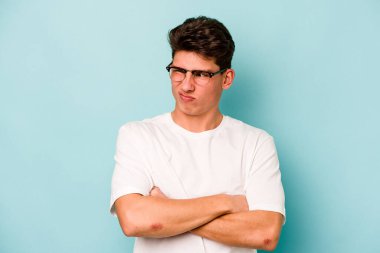 Kafkasyalı genç adam mavi arka planda izole edilmiş şüpheli, belirsiz, seni muayene ediyor..