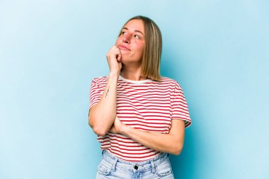 Kafkasyalı genç kadın mavi arka planda izole edilmiş düşünüyor ve yukarı bakıyor, yansıtıyor, düşünüyor, bir fantezi kuruyor..