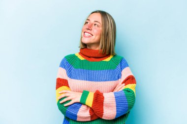 Mavi arka planda izole edilmiş genç beyaz kadın hedeflerine ve amaçlarına ulaşma hayali kuruyor.