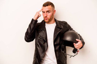 Motosiklet kasklı genç beyaz arka planda izole edilmiş beyaz bir beyaz adam şakağı işaret ediyor, düşünüyor ve bir göreve odaklanıyor..