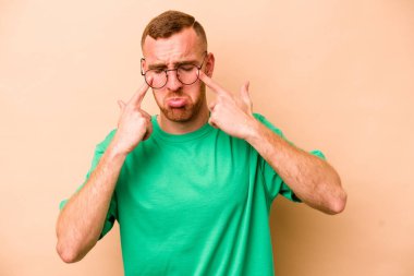 Beyaz tenli genç adam bej arka planda izole edilmiş ağlıyordu, bir şeyden mutsuzdu, ıstırap ve kafa karışıklığı vardı..