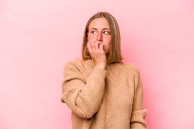 Pembe arka planda izole edilmiş, tırnak yiyen, gergin ve endişeli bir beyaz kadın..