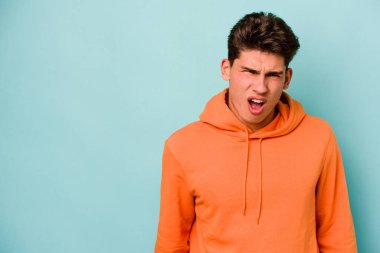 Kafkasyalı genç adam mavi arka planda izole edilmiş. Çok kızgın, öfkeli, hayal kırıklığına uğramış..