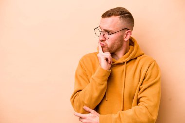 Beyazlı genç adam bej arka planda izole edilmiş şüpheli ve şüpheci bir ifadeyle yana bakıyor..