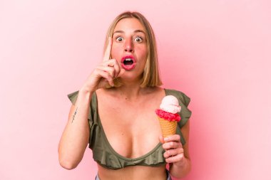 Bikini giyen ve elinde pembe arka planda izole edilmiş dondurma tutan beyaz bir kadın..