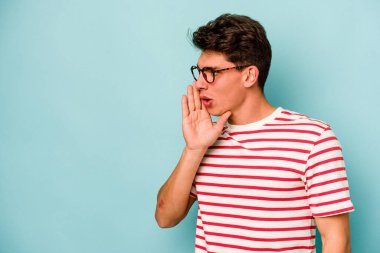 Mavi arka planda izole edilmiş genç beyaz bir adam gizli bir sıcak fren haberi veriyor ve yana bakıyor.