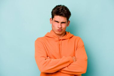 Kafkasyalı genç adam mavi arka planda izole edilmiş hoşnutsuzca kaşlarını çatmış, kollarını kavuşturmuş..