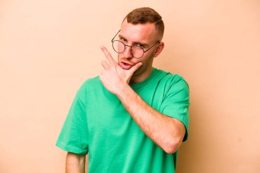 Beyazlı genç bir adam bej arka planda izole edilmiş. Bir strateji planlıyor, bir iş yolu düşünüyor..