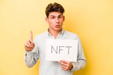 Elinde NFT levhası olan beyaz bir adam sarı arka planda izole edilmiş. Harika bir fikri var. Yaratıcılık kavramı..