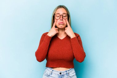 Kafkasyalı genç bir kadın mavi arka planda izole edilmiş, ağlıyor, bir şeyden memnun değil, acı ve kafa karışıklığı konsepti..