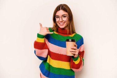 Beyaz arka planda izole edilmiş kahve taşıyan beyaz saçlı genç bir kadın cep telefonu hareketini parmaklarıyla gösteriyor..