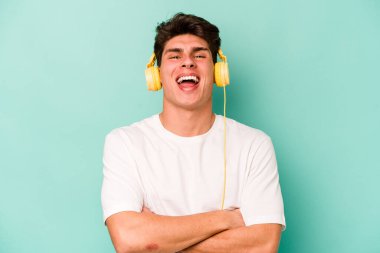 Mavi arka planda izole edilmiş müzik dinleyen beyaz bir adam gülüyor ve eğleniyor..