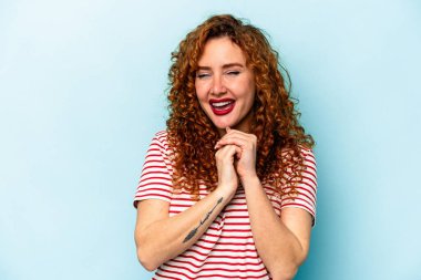 Mavi arka planda izole edilmiş genç beyaz kadın ellerini çenesinin altında tutuyor ve mutlu bir şekilde yan tarafa bakıyor..