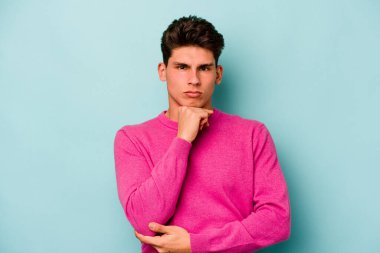 Kafkasyalı genç adam mavi arka planda izole edilmiş şüpheli, belirsiz, seni muayene ediyor..