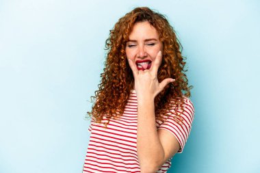 Mavi arka planda izole edilmiş genç kızıl saçlı kadın parmaklarıyla kaya hareketi gösteriyor.