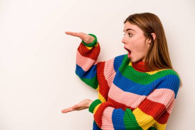 Beyaz arka planda izole genç beyaz kadın şok ve hayret içinde elleri arasında bir kopya alanı tutuyor.