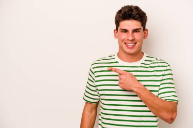 Beyaz arka planda izole edilmiş genç beyaz bir adam gülümsüyor ve boş alanda bir şeyler gösteriyor..