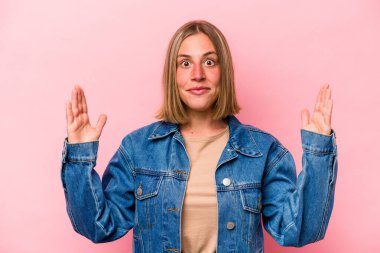 Pembe arka planda izole edilmiş genç beyaz bir kadın işaret parmaklarıyla küçük bir şey tutuyor, gülümsüyor ve kendinden emin..