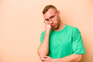 Bej arka planda izole edilmiş, üzgün ve dalgın hisseden, fotokopi alanına bakan genç beyaz bir adam..