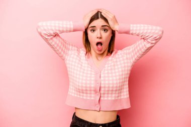 Pembe arka planda izole edilmiş genç beyaz kadın şaşırmış ve şok olmuş..