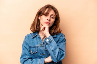 Beyaz tenli genç bir kadın, bej arka planda izole edilmiş şüpheli, belirsiz, seni muayene ediyor..