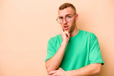 Beyazlı genç adam bej arka planda izole edilmiş şüpheli ve şüpheci bir ifadeyle yana bakıyor..