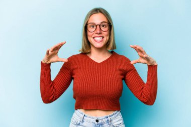 Kafkasyalı genç bir kadın mavi arka planda izole edilmiş. Elinde avuç içi olan bir şeyle kameraya sunuyor..