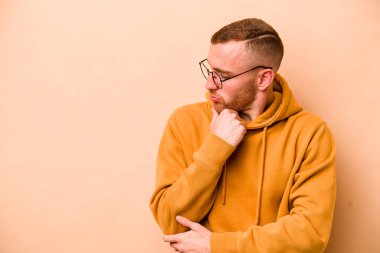 Beyazlı genç adam bej arka planda izole edilmiş şüpheli ve şüpheci bir ifadeyle yana bakıyor..