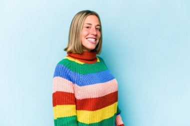 Kafkasyalı genç bir kadın mavi arka planda izole edilmiş. Kendine güvenen, ellerini kalçasında tutan..