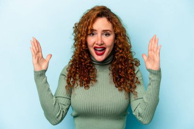 Mavi arka planda izole edilmiş genç, beyaz bir kadın hoş bir sürprizle karşılaşıyor, heyecanlı ve el kaldırıyor..