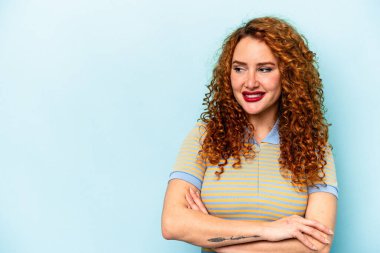 Mavi arka planda izole edilmiş genç, beyaz kadın kollarını kavuşturarak gülümsüyor..