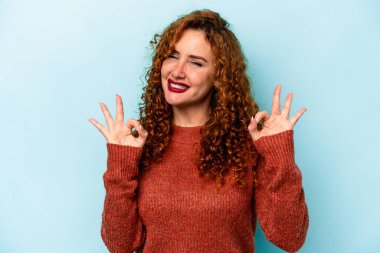 Genç, beyaz, mavi arka planda izole edilmiş, neşeli ve kendinden emin bir kadın..