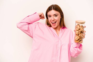 Beyaz arka planda izole edilmiş kurabiye kavanozu tutan beyaz bir kadın zafer kazandıktan sonra yumruğunu kaldırıyor..