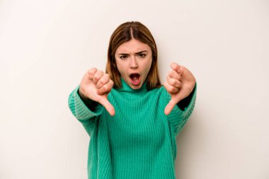 Beyaz arka planda izole edilmiş genç beyaz kadın baş parmağını aşağı gösteriyor ve hoşlanmadığını ifade ediyor..