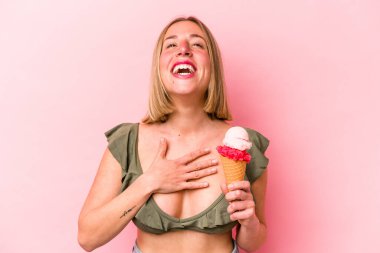 Bikini giyen ve pembe arka planda izole edilmiş dondurma tutan beyaz bir kadın kahkahalar atıyor..