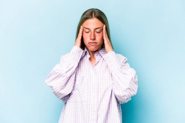 Mavi arka planda izole edilmiş genç beyaz kadın şakaklara dokunuyor ve baş ağrısı çekiyor..