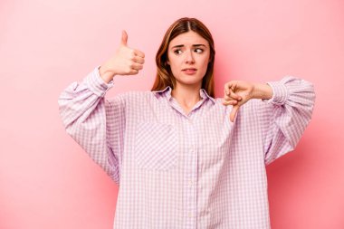 Pembe arka planda izole edilmiş genç beyaz kadın baş parmağını kaldırıyor ve baş parmağını aşağı gösteriyor, zor seçim kavramı.