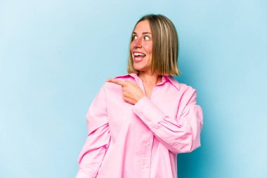 Mavi arka planda soyutlanmış genç beyaz kadın gülümseyen, neşeli ve keyifli bir tarafa bakıyor..