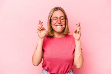 Pembe arka planda izole edilmiş beyaz bir kadın şans getirsin diye dua ediyor.