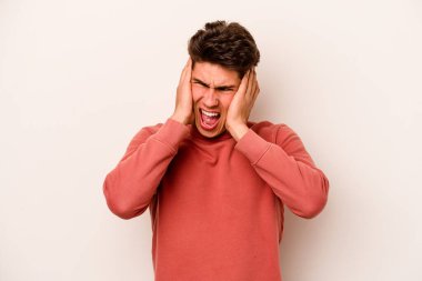 Beyaz arka planda izole edilmiş genç beyaz bir adam kulakları kulaklarıyla kapatıyor ve çok ses duymamaya çalışıyor..