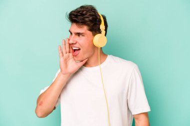 Mavi arka planda izole edilmiş müzik dinleyen genç beyaz adam bağırıyor ve avuç içini açık tutuyor..