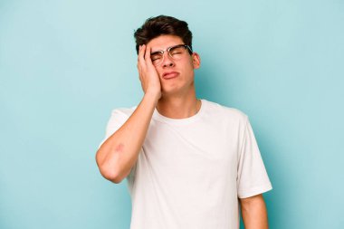 Kafkasyalı genç adam mavi arka planda izole edilmiş. Yorgun ve uykulu. Elini başının üstünde tutuyor..