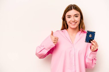 Beyaz arka planda izole edilmiş genç, gayri resmi beyaz kadın gülümsüyor ve başparmağını kaldırıyor.