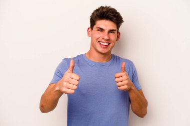 Beyaz arka planda izole edilmiş genç beyaz bir adam iki parmağını da kaldırıyor, gülümsüyor ve kendinden emin..