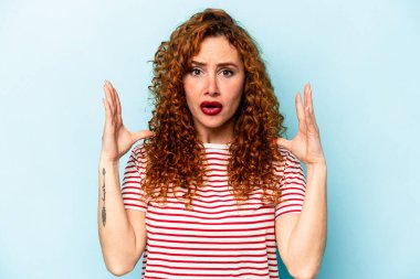 Genç, beyaz, mavi arka planda izole edilmiş kadın şaşırmış ve şok olmuş..