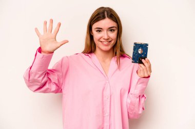 Beyaz arka planda izole edilmiş genç, gayri resmi beyaz kadın gülümseyerek beş numarayı parmaklarıyla gösteriyor..