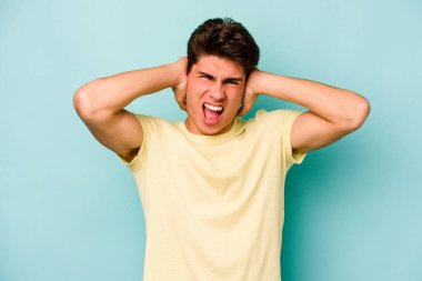 Kafkasyalı genç adam mavi arka planda izole edilmiş kulakları kulaklarıyla kapatıyor çok fazla ses duymamaya çalışıyor..