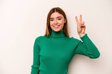 Beyaz arka planda izole edilmiş genç beyaz kadın neşeli ve kaygısız parmakları olan bir barış sembolü gösteriyor..