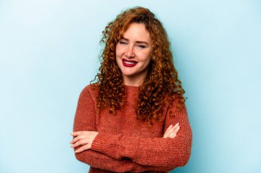 Mavi arka planda kendini güvende hisseden, kararlılıkla kollarını kavuşturan genç beyaz bir kadın..